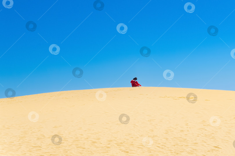 Скачать одинокая туристка вытряхивает песок из своих ботинок на вершине дюны Сарыкум, Дагестан фотосток Ozero