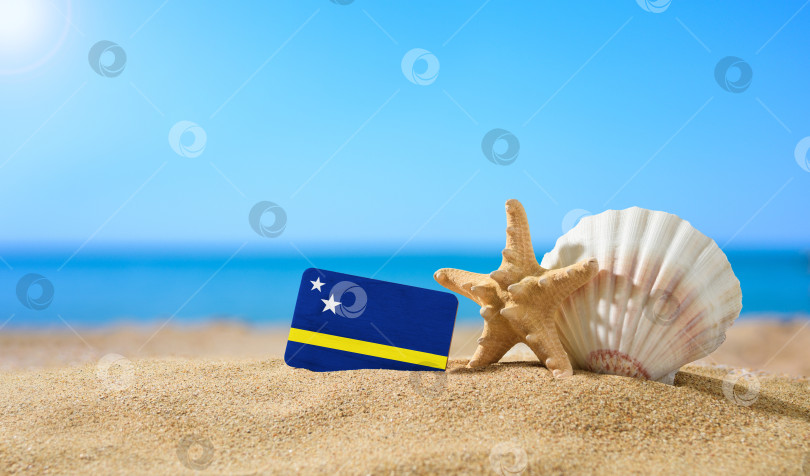 Скачать Тропический пляж с ракушками и флагом Кюрасао. Концепция райского отдыха на пляжах Кюрасао. фотосток Ozero