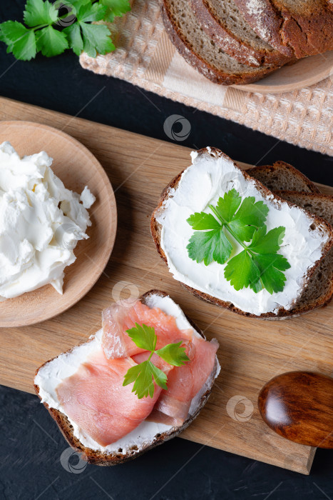 Скачать Домашний хлеб на деревянной разделочной доске с творожным сыром и лососем. Украшен зеленью фотосток Ozero