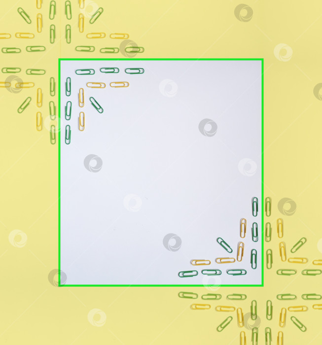 Скачать Абстрактный фон, белый квадрат в светло-желтой рамке с принтом из зеленых и желтых скрепок по противоположным углам. фотосток Ozero