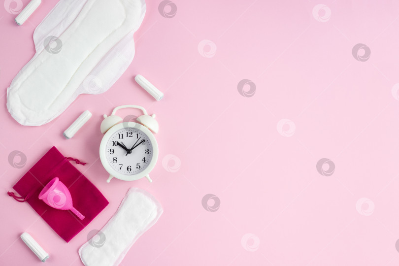 Скачать Предметы интимной женской гигиены и белый будильник на розовом фоне. Понятие о женской менструации. Выборочный фокус, пространство для копирования фотосток Ozero
