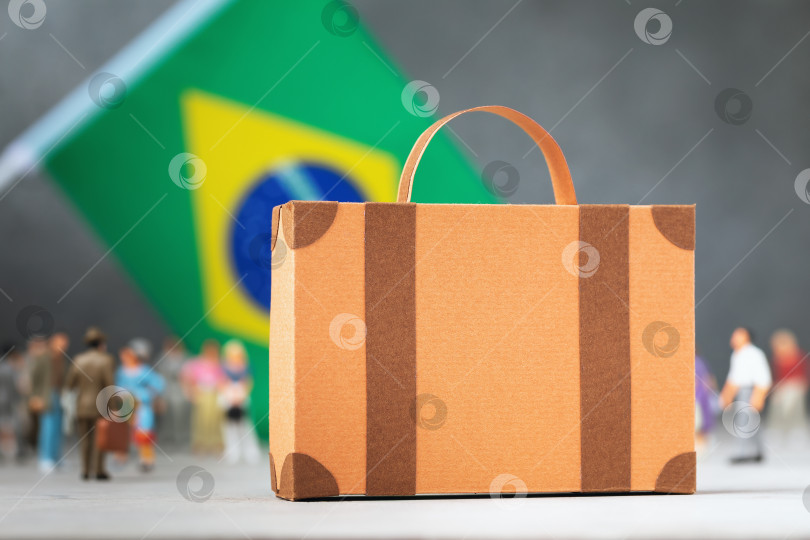 Скачать Картонный чемодан, пластмассовые игрушечные человечки и флаг на абстрактном фоне, концепция на тему переезда в Бразилию фотосток Ozero