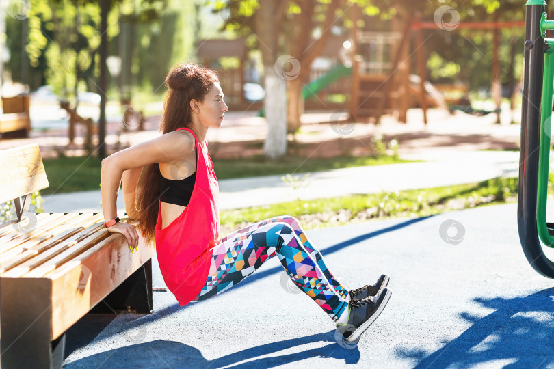 Скачать Девочка выполняет упражнение отжимания от скамейки на детской площадке летним солнечным утром. Концепция спорта фотосток Ozero