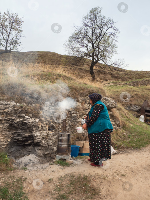 Скачать Народы Кавказа. Пожилая дагестанская (аварская) дама. Гостеприимная хозяйка аутентичного кафе позирует у очага, где готовится вкусный чай. фотосток Ozero