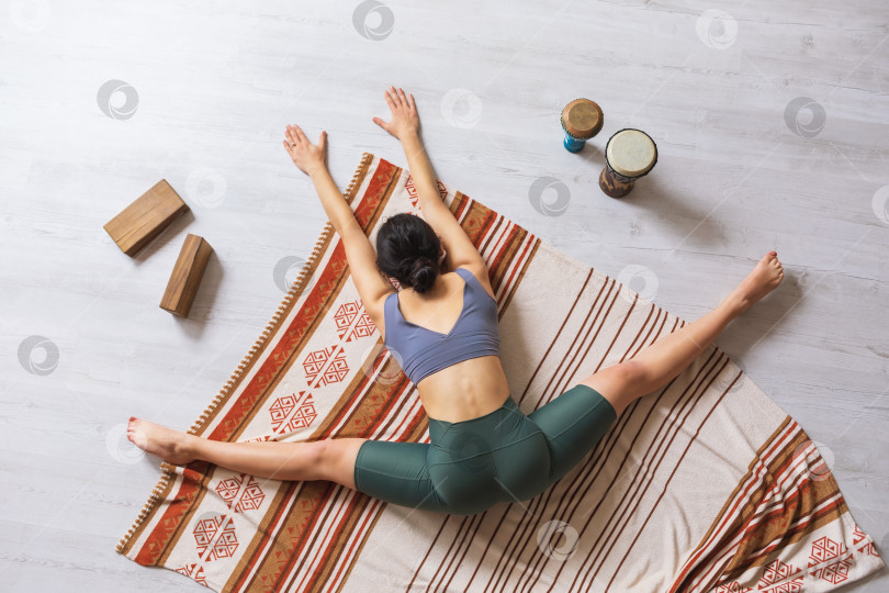 Скачать Женщина в спортивной одежде, занимающаяся йогой, выполняет упражнение самоканасана, сидя на одеяле, поперечный разрез с наклоном тела вперед фотосток Ozero