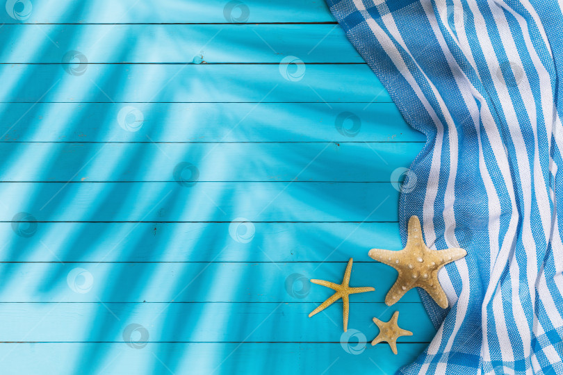 Скачать Полотенце и морские звезды на синем деревянном фоне с пробелом для копирования и тенью от пальмового листа фотосток Ozero