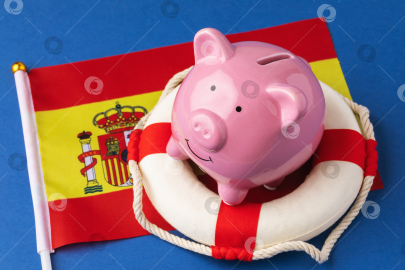 Скачать Копилка, спасательный круг и флаг на синем фоне, концепция на тему спасения испанской экономики фотосток Ozero