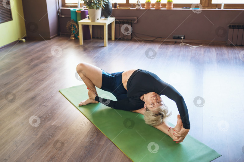 Скачать Женщина, ведущая здоровый образ жизни и практикующая йогу, выполняет упражнение паривритта джана ширшасана, наклон головы к коленям, тренируется одна в спортивной одежде, лежа на коврике в студии фотосток Ozero