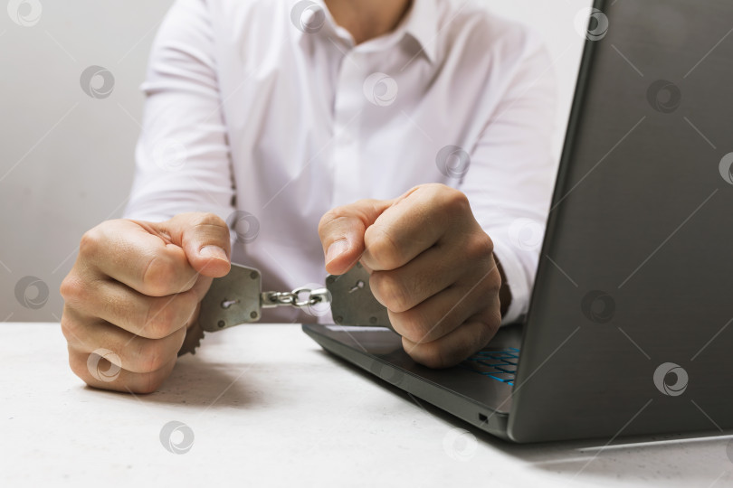Скачать Мужчина в наручниках возле ноутбука, концепция на тему компьютерных преступлений фотосток Ozero