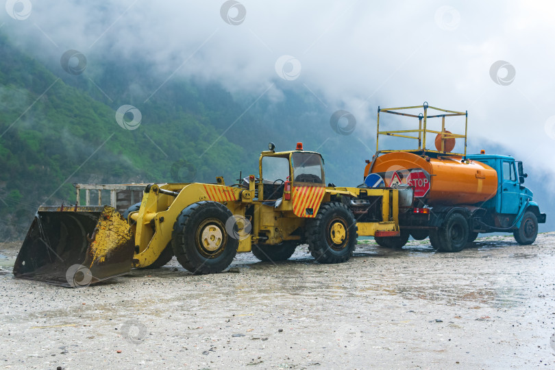 Скачать тяжелая дорожная техника для разгребания оползней стоит на обочине дороги в горной местности во время штормовой погоды фотосток Ozero