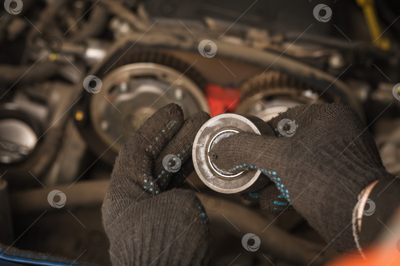 Скачать Автомеханик проверяет состояние ролика натяжителя ремня ГРМ легкового автомобиля фотосток Ozero