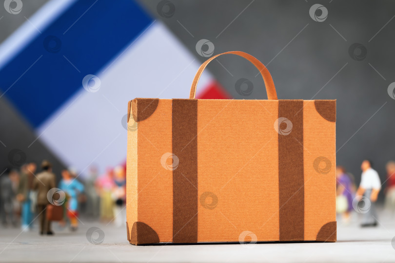 Скачать Картонный чемодан, пластмассовые игрушечные человечки и флаг на абстрактном фоне, концепция на тему переезда или миграции во Францию фотосток Ozero