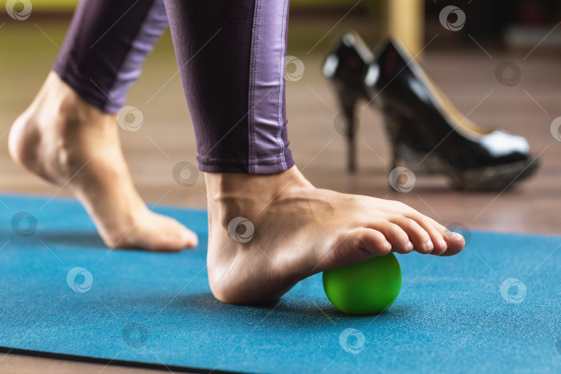 Скачать Женщина выполняет расслабляющие упражнения мышц стопы с массажным шариком, для профилактики усталости ног после ношения обуви на высоком каблуке фотосток Ozero