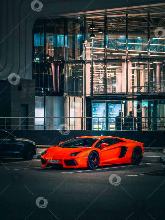 Скачать Оранжевый суперкар Lamborghini стоит ночью у банка. фотосток Ozero