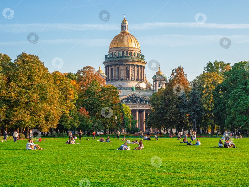 Скачать Зеленая лужайка перед собором с отдыхающими людьми. Осенний пейзаж с Исаакиевским собором, культовой достопримечательностью Санкт-Петербурга, Россия. фотосток Ozero