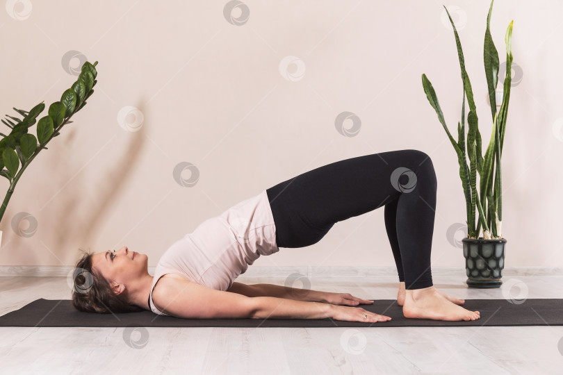 Скачать Женщина, ведущая здоровый образ жизни и практикующая йогу, выполняет упражнение дви пада питхасана, поза полумоста, тренируется одна в комнате у стены фотосток Ozero