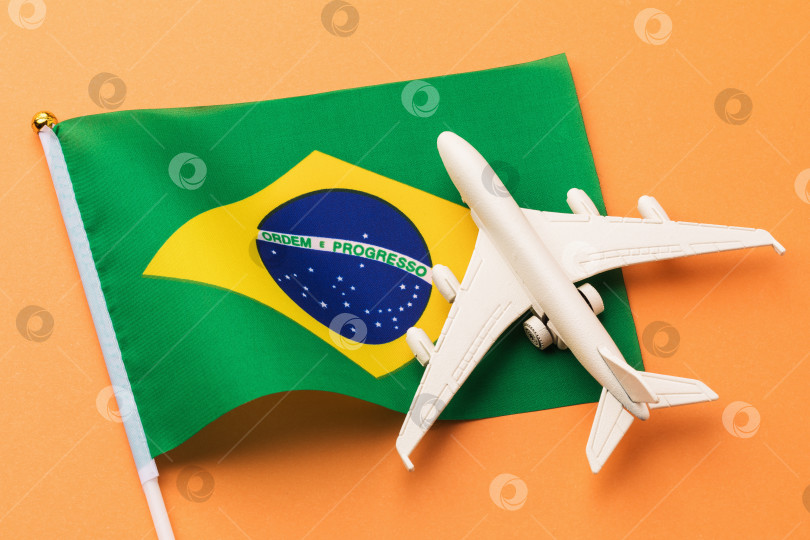 Скачать Бразильский флаг и игрушечный самолет на цветном фоне, концепция полета в Бразилию, вид сверху фотосток Ozero