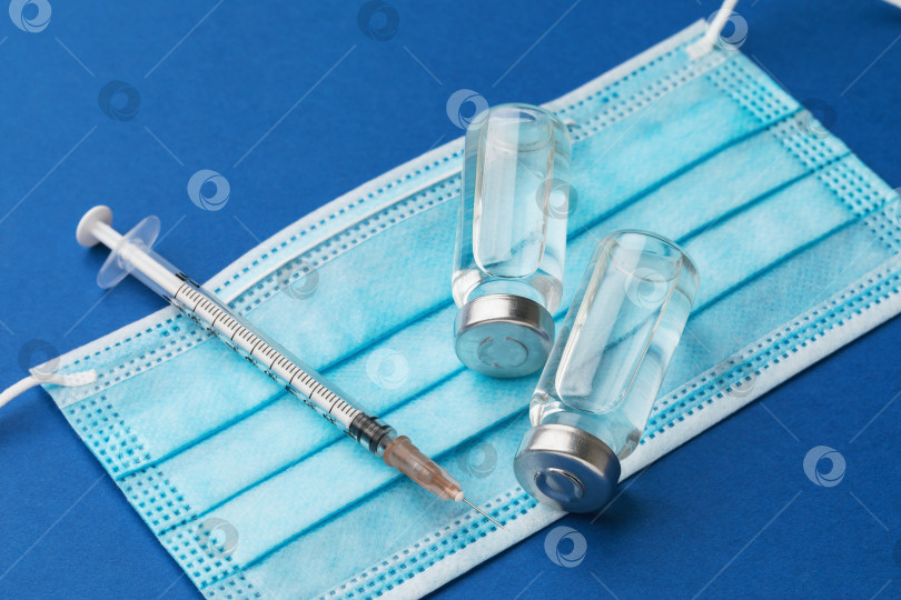 Скачать Одноразовый шприц, раствор для инъекций и медицинская маска на синем фоне, концепция на тему вакцинации против коронавируса фотосток Ozero