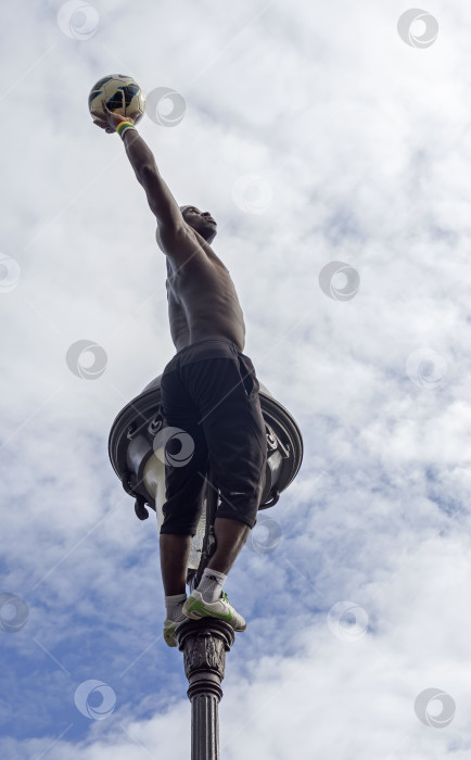 Скачать Акробат с мячом, висящим на верхушке фонарного столба. фотосток Ozero
