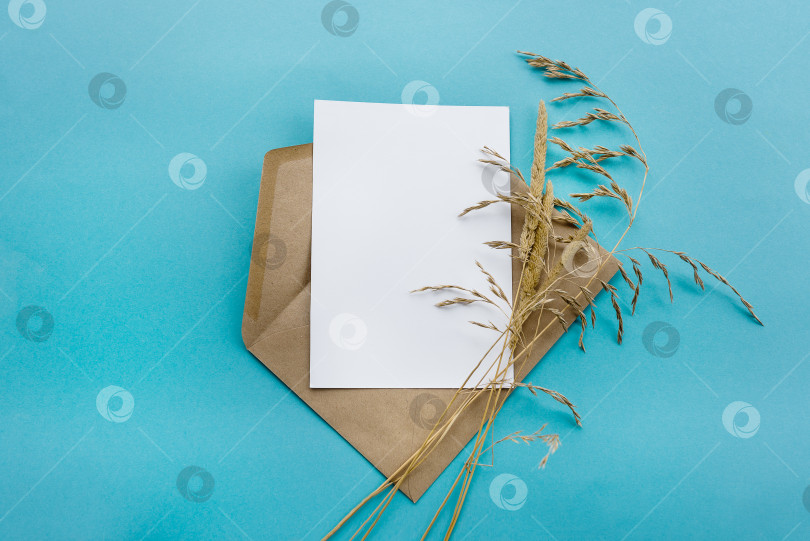 Скачать Конверт из крафт-бумаги с белой пустой карточкой на синем фоне. Подготовка открытки фотосток Ozero