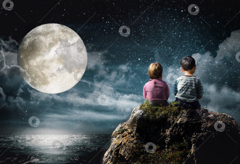 Скачать Маленькие мальчик и девочка сидят на скале над морем и смотрят на луну и звезды фотосток Ozero