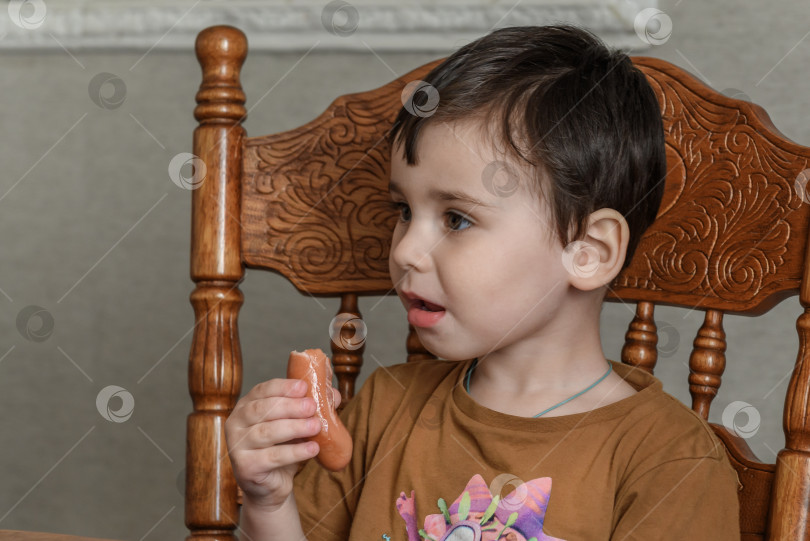 Скачать Маленький мальчик ест сосиску за столом фотосток Ozero