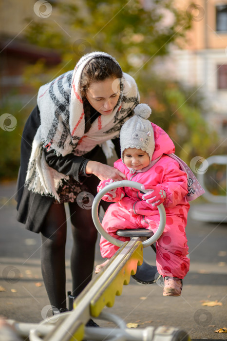 Скачать молодая мама с маленькой дочкой на качелях во дворе осенью фотосток Ozero