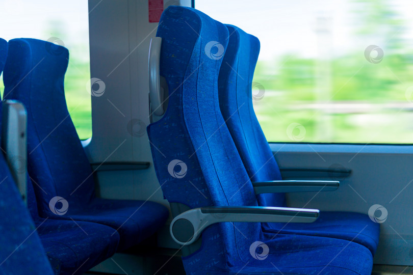 Скачать интерьер вагона пригородного пассажирского поезда, ряд стульев и размытый движением пейзаж за окном. фотосток Ozero