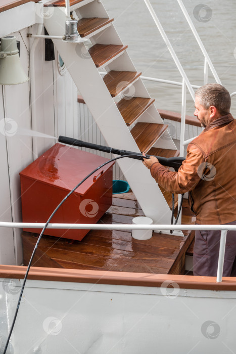 Скачать Россия, Санкт-Петербург, 10 сентября 2022 года: Мужчина моет палубу яхты шлангом фотосток Ozero