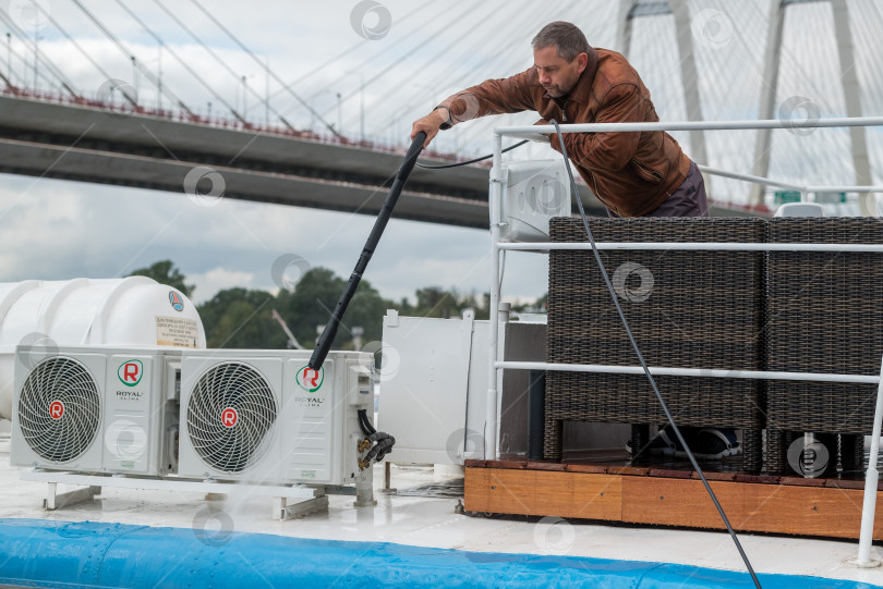 Скачать Россия, Санкт-Петербург, 10 сентября 2022 года: Мужчина моет палубу яхты из шланга фотосток Ozero