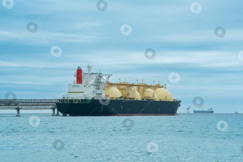 Скачать танкер-перевозчик сжиженного природного газа во время погрузки на морском терминале сжиженного природного газа, вдалеке в море виден терминал для экспорта нефти фотосток Ozero