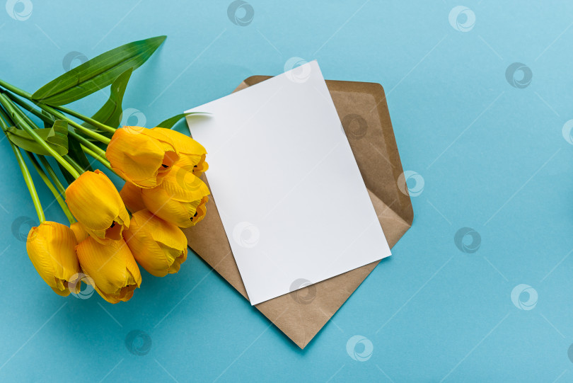 Скачать Конверт из крафт-бумаги и белая пустая открытка с желтыми тюльпанами на синем фоне. Подготовка открытки фотосток Ozero