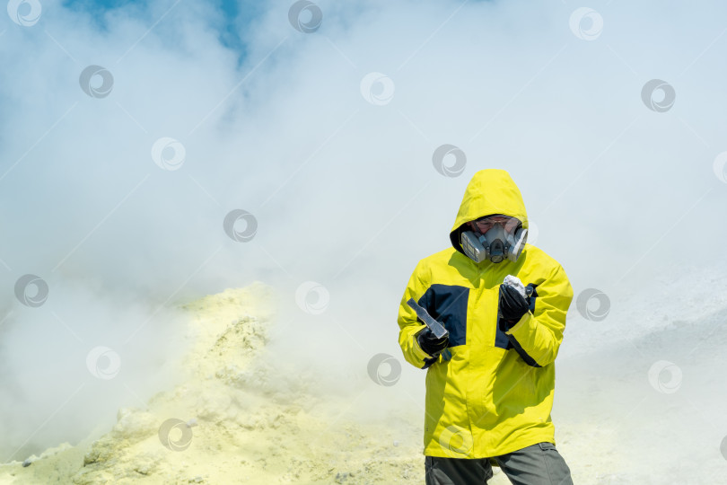 Скачать мужчина-вулканолог на склоне вулкана среди паров фумаролы исследует образец минерала фотосток Ozero