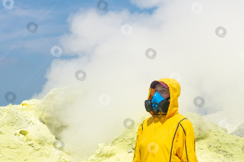 Скачать женщина-вулканолог с геологическим молотком и в респираторе на фоне дымящейся фумаролы на склоне вулкана фотосток Ozero