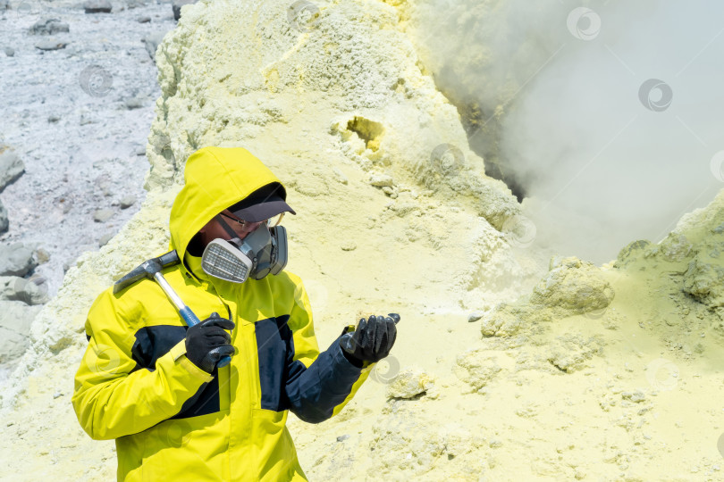 Скачать мужчина-вулканолог с геологическим молотком и в респираторе на склоне близлежащего вулкана среди токсичных паров фотосток Ozero