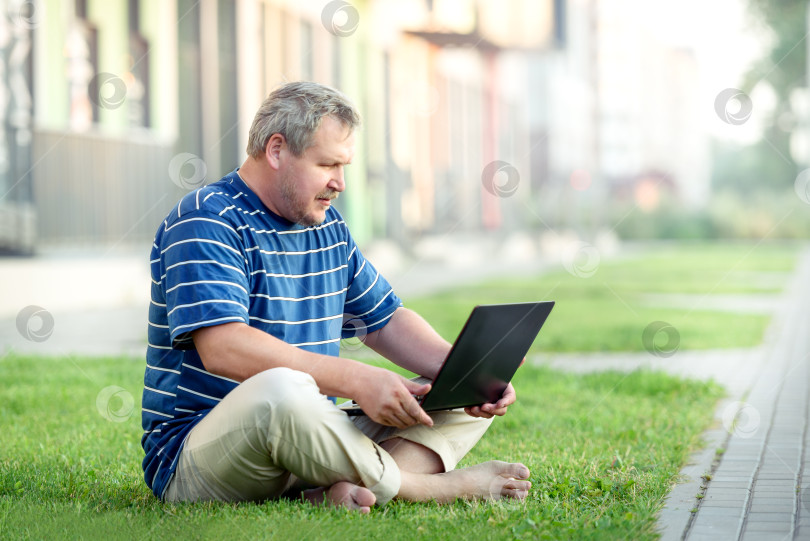 Скачать Красивый взрослый мужчина сидит на лужайке в городе с ноутбуком. О современной городской жизни. фотосток Ozero