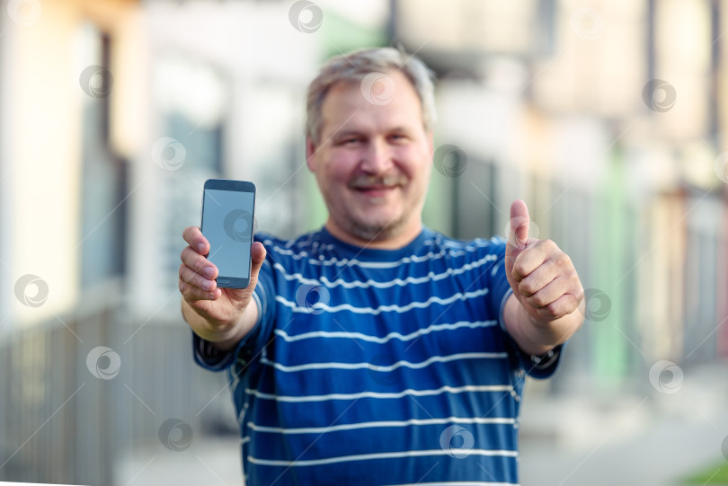 Скачать Крупный план руки счастливого мужчины, показывающей пустой экран смартфона на улице фотосток Ozero