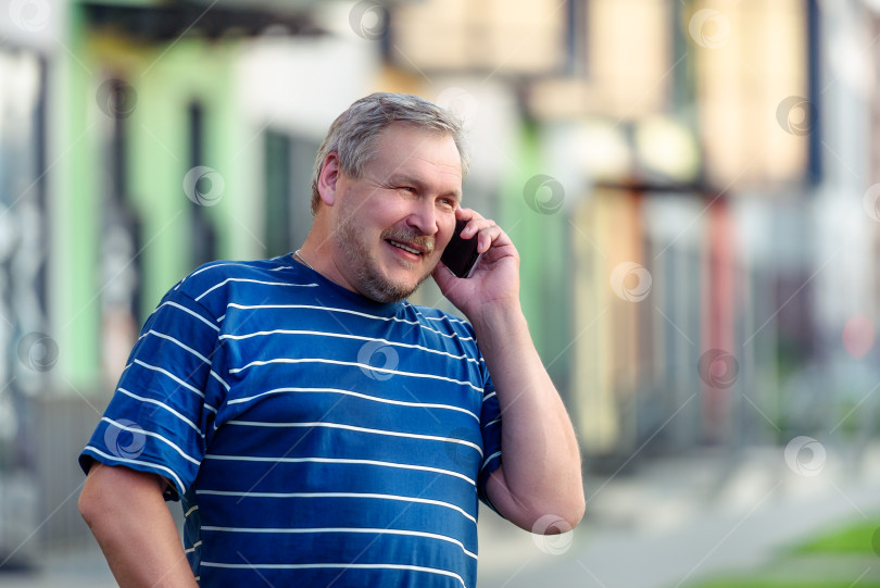 Скачать Мужчина радостно разговаривает по смартфону, прогуливаясь по улице фотосток Ozero