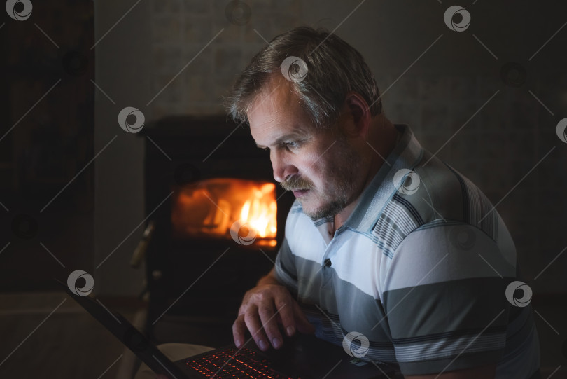 Скачать мужчина просматривает контент на ноутбуке вечером дома у камина фотосток Ozero