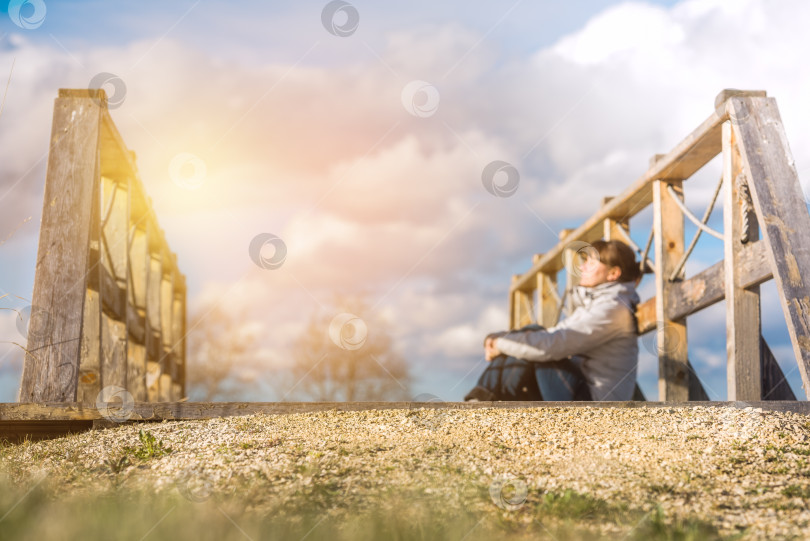 Скачать молодая женщина сидит на мосту на природе, солнечно. фотосток Ozero