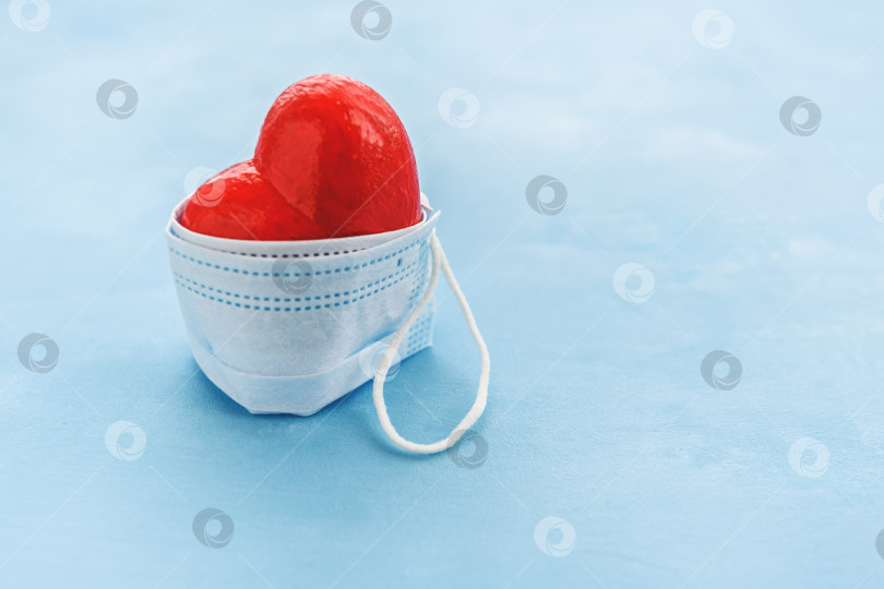 Скачать Красное сердце, защищенное медицинской маской на синем фоне. фотосток Ozero