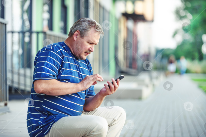Скачать Взрослый красивый мужчина пользуется смартфоном - концептом коммуникации и технологий. Мужчина разговаривает по телефону в городе фотосток Ozero