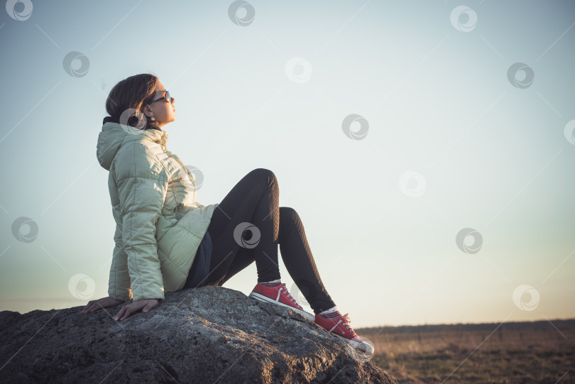 Скачать девочка-подросток сидит на большом камне в поле и смотрит на закат фотосток Ozero