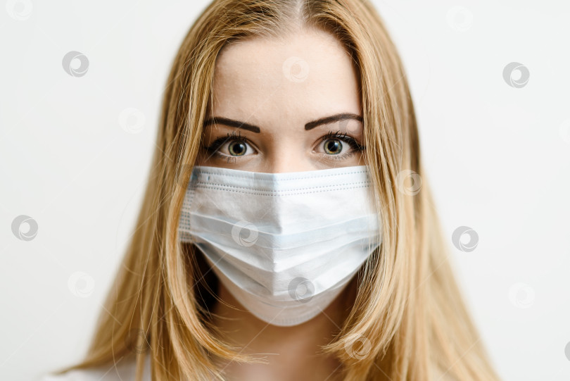 Скачать Портрет молодой девушки в медицинской маске на фоне белой стены. фотосток Ozero