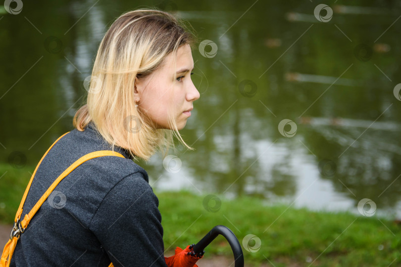Скачать Молодая девушка, сидящая на траве в парке у озера с красным зонтиком - вид крупным планом сзади фотосток Ozero
