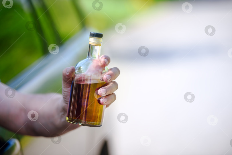 Скачать Алкоголь, бутылка, автомобиль и концепция вождения в нетрезвом виде - человек держит в руке бутылку с алкогольным напитком, управляя автомобилем. Подтянутый фотосток Ozero