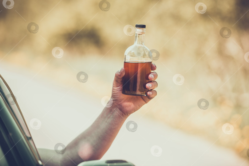 Скачать Алкоголь, бутылка, автомобиль и концепция вождения в нетрезвом виде - человек держит в руке бутылку с алкогольным напитком, управляя автомобилем. Подтянутый фотосток Ozero
