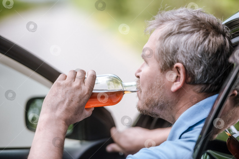 Скачать Мужчина за рулем автомобиля с бутылкой алкогольного напитка. Концепция "Не пей и не садись за руль" фотосток Ozero