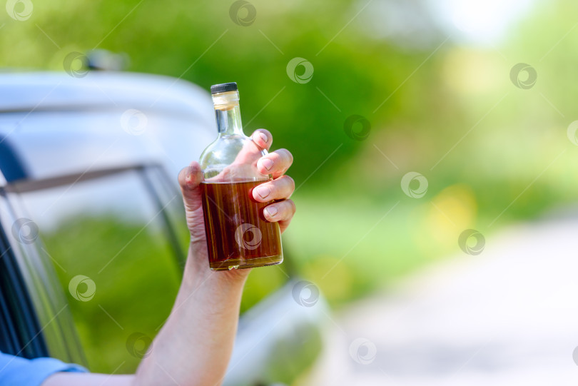 Скачать Алкоголь, бутылка, автомобиль и понятие вождения в нетрезвом виде - человек держит в руке бутылку с алкогольным напитком, управляя автомобилем. Подтянутый фотосток Ozero