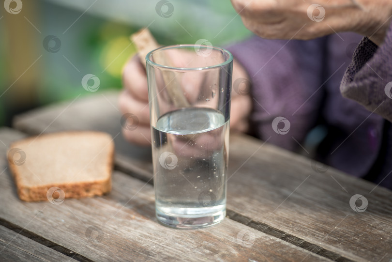 Скачать Старуха пьет воду и ест хлеб за старым деревянным столом в саду фотосток Ozero